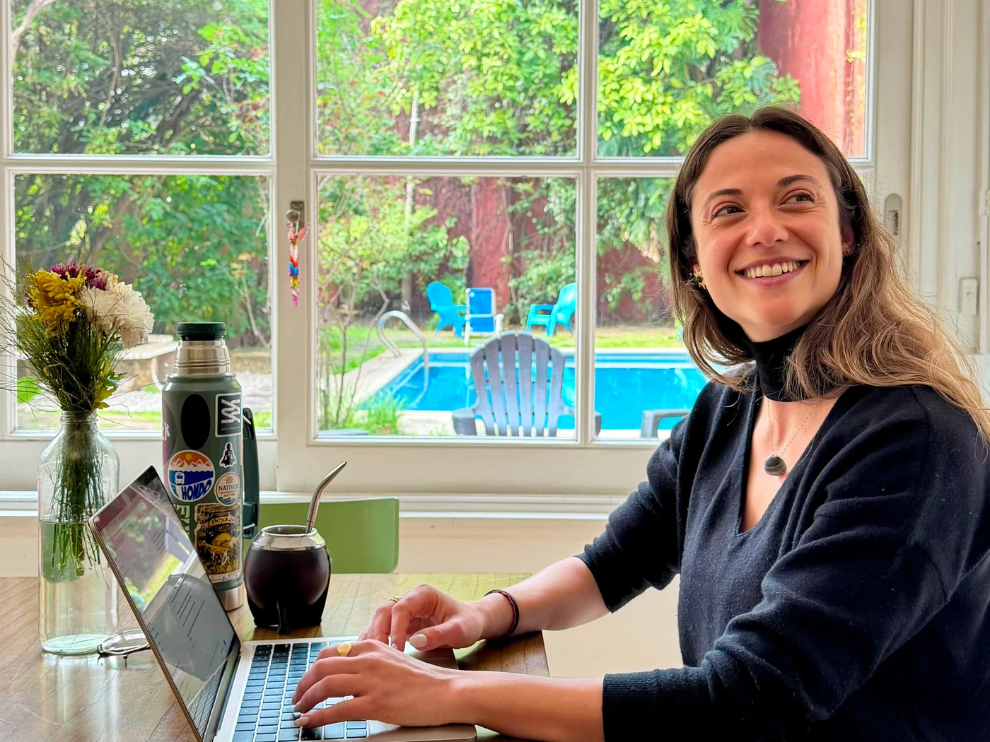 Una miembro trabajando con su notebook y el mate, con el jardín y la pileta de fondo
